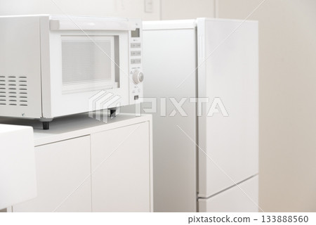 A clean white mini kitchen with a refrigerator and microwave 133888560