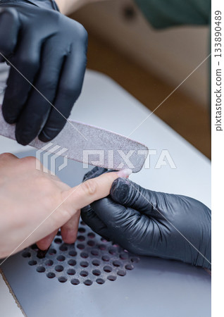 Detailed view of professional manicure procedure with nail care tools and hands in focus. Detailed view of professional manicure procedure with nail care tools and hands in focus. 133890489