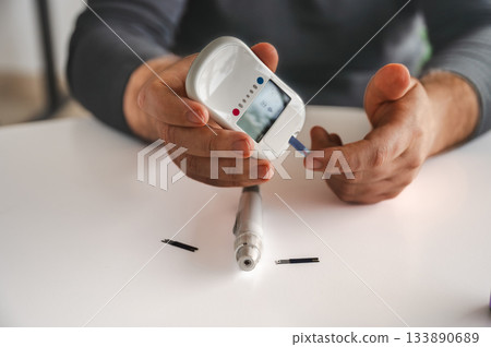 Close-up of a man's hands using a lancet on his finger to test blood glucose level. Concept of diabetes care, glycemia monitoring, and health management. 133890689
