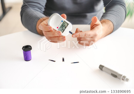 Close-up of a man's hands using a lancet on his finger to test blood glucose level. Concept of diabetes care, glycemia monitoring, and health management. 133890695