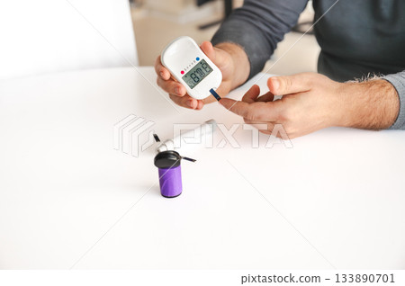 Close-up of a man's hands using a lancet on his finger to test blood glucose level. Concept of diabetes care, glycemia monitoring, and health management. Close-up of a man's hands using a lancet on his finger to test blood glucose level. Concept of diabetes care, glycemia monitoring, and health management. 133890701