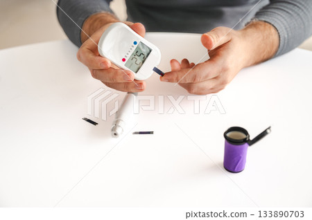 Close-up of a man's hands using a lancet on his finger to test blood glucose level. Concept of diabetes care, glycemia monitoring, and health management. 133890703