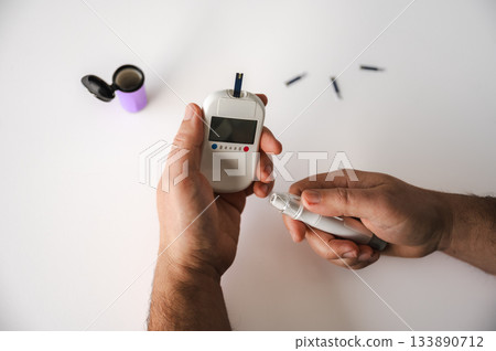 Close-up of a man's hands using a lancet on his finger to test blood glucose level. Concept of diabetes care, glycemia monitoring, and health management. 133890712