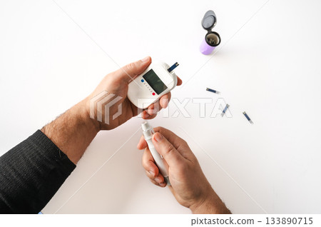 Close-up of a man's hands using a lancet on his finger to test blood glucose level. Concept of diabetes care, glycemia monitoring, and health management. 133890715
