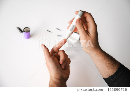 Close-up of a man's hands using a lancet on his finger to test blood glucose level. Concept of diabetes care, glycemia monitoring, and health management. Close-up of a man's hands using a lancet on his finger to test blood glucose level. Concept of diabetes care, glycemia monitoring, and health management. 133890716