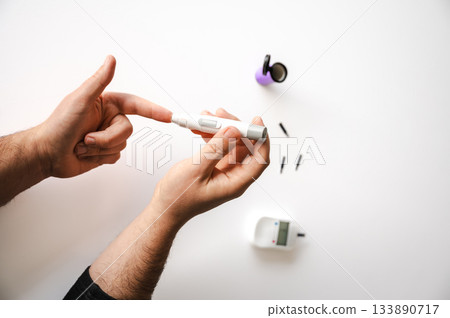 Close-up of a man's hands using a lancet on his finger to test blood glucose level. Concept of diabetes care, glycemia monitoring, and health management. 133890717