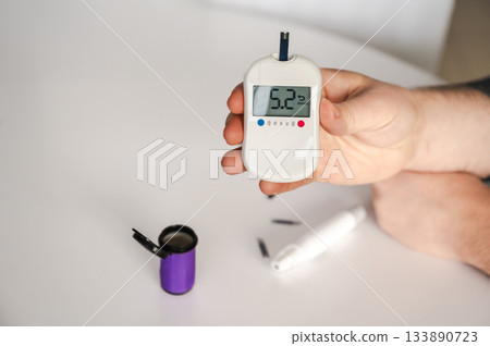 Close-up of a man's hands using a lancet on his finger to test blood glucose level. Concept of diabetes care, glycemia monitoring, and health management. 133890723