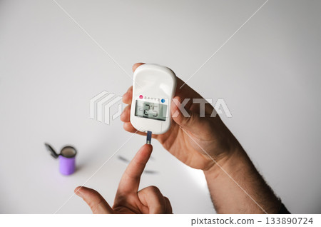 Close-up of a man's hands using a lancet on his finger to test blood glucose level. Concept of diabetes care, glycemia monitoring, and health management. 133890724