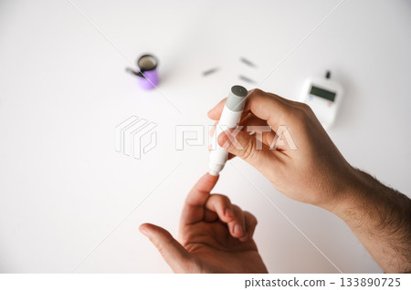 Close-up of a man's hands using a lancet on his finger to test blood glucose level. Concept of diabetes care, glycemia monitoring, and health management. 133890725