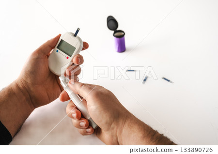 Close-up of a man's hands using a lancet on his finger to test blood glucose level. Concept of diabetes care, glycemia monitoring, and health management. 133890726