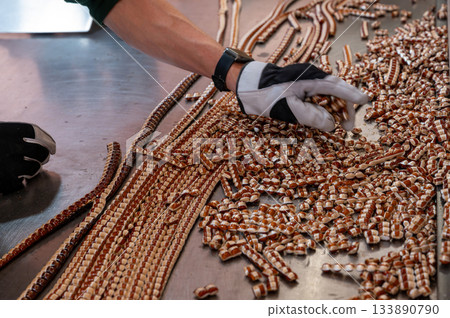 Close-up view of caramel candy making in a factory, showing warm melted sugar being shaped and crafted into sweet treats. Close-up view of caramel candy making in a factory, showing warm melted sugar being shaped and crafted into sweet treats. 133890790
