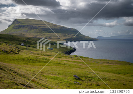 Low clouds hang over the remote Scandinavian island of Nolsoy in the Faroe Islands. Dramatic landscape of grass covered mountains and basalt columns along the coastline. High quality photo 133890795