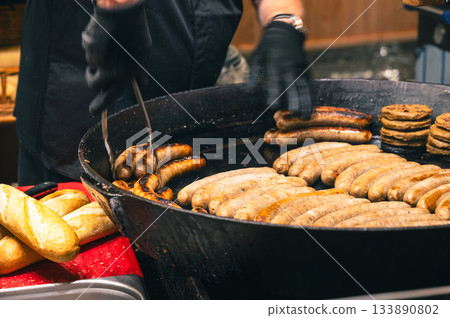 Delicious grilled sausage with spices and fresh rosemary cooking on a metal grate, capturing the warm and festive atmosphere of a Christmas fair. 133890802