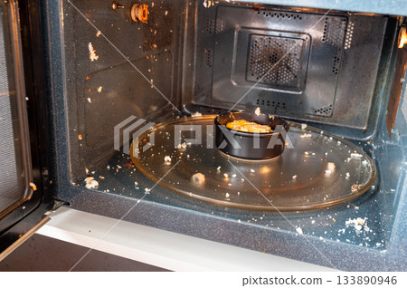 Close-up of a microwave interior with traces of an exploded egg - pieces of shell and egg splattered inside, showing a kitchen accident or cooking fail. Close-up of a microwave interior with traces of an exploded egg - pieces of shell and egg splattered inside, showing a kitchen accident or cooking fail. 133890946