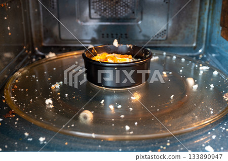 Close-up of a microwave interior with traces of an exploded egg - pieces of shell and egg splattered inside, showing a kitchen accident or cooking fail. 133890947