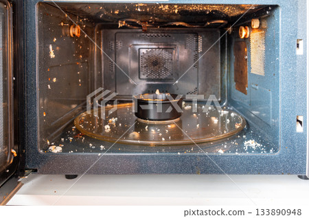 Close-up of a microwave interior with traces of an exploded egg - pieces of shell and egg splattered inside, showing a kitchen accident or cooking fail. Close-up of a microwave interior with traces of an exploded egg - pieces of shell and egg splattered inside, showing a kitchen accident or cooking fail. 133890948