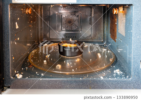 Close-up of a microwave interior with traces of an exploded egg - pieces of shell and egg splattered inside, showing a kitchen accident or cooking fail. 133890950