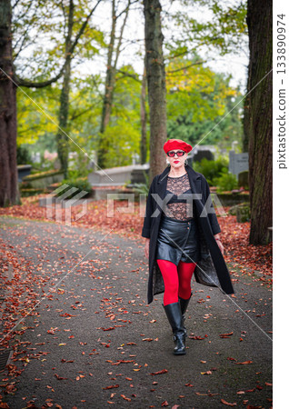 Elegant, well-groomed woman with fashionable style walking in an autumn park on a cloudy day. She wears a red beret, red lipstick, and matching red tights, looking confident and sophisticated. 133890974