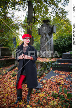 Elegant, well-groomed woman with fashionable style walking in an autumn park on a cloudy day. She wears a red beret, red lipstick, and matching red tights, looking confident and sophisticated. 133890975