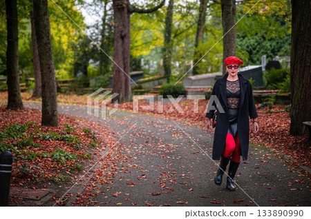 Elegant, well-groomed woman with fashionable style walking in an autumn park on a cloudy day. She wears a red beret, red lipstick, and matching red tights, looking confident and sophisticated. Elegant, well-groomed woman with fashionable style walking in an autumn park on a cloudy day. She wears a red beret, red lipstick, and matching red tights, looking confident and sophisticated. 133890990
