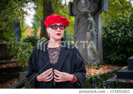 Elegant, well-groomed woman with fashionable style walking in an autumn park on a cloudy day. She wears a red beret, red lipstick, and matching red tights, looking confident and sophisticated. Elegant, well-groomed woman with fashionable style walking in an autumn park on a cloudy day. She wears a red beret, red lipstick, and matching red tights, looking confident and sophisticated. 133891001