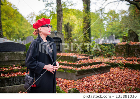Elegant, well-groomed woman with fashionable style walking in an autumn park on a cloudy day. She wears a red beret, red lipstick, and matching red tights, looking confident and sophisticated. Elegant, well-groomed woman with fashionable style walking in an autumn park on a cloudy day. She wears a red beret, red lipstick, and matching red tights, looking confident and sophisticated. 133891030