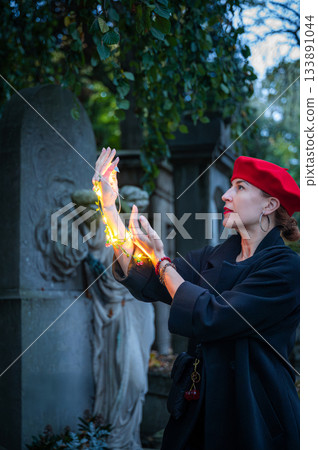 Elegant, well-groomed woman with fashionable style walking in an autumn park on a cloudy day. She wears a red beret, red lipstick, and matching red tights, looking confident and sophisticated. 133891044
