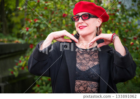 Elegant, well-groomed woman with fashionable style walking in an autumn park on a cloudy day. She wears a red beret, red lipstick, and matching red tights, looking confident and sophisticated. Elegant, well-groomed woman with fashionable style walking in an autumn park on a cloudy day. She wears a red beret, red lipstick, and matching red tights, looking confident and sophisticated. 133891062