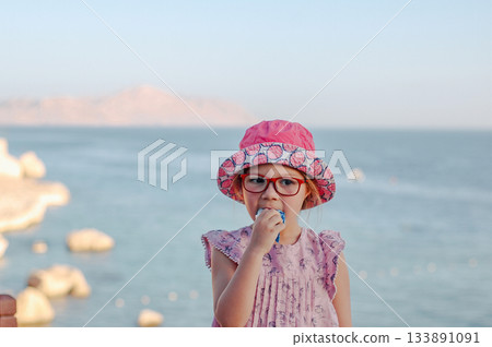 Little adorable child girl enjoying summer in the beach. Eating icecream Little adorable child girl enjoying summer in the beach. Eating icecream 133891091
