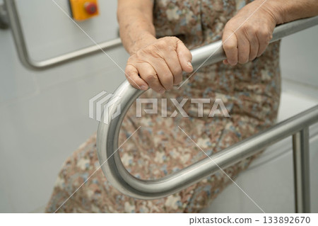 Asian elderly woman patient use toilet support rail in bathroom. 133892670
