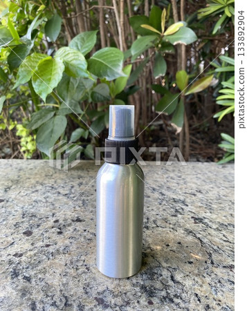 Spray Bottle by Green Bushes on Stone Surface Spray Bottle by Green Bushes on Stone Surface 133892904