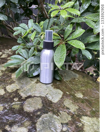 Spray Bottle on Wet Stone with Raindrops on Leaves 133892908