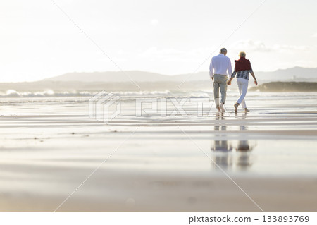 Senior couple walking hand in hand enjoying beach sunset Senior couple walking hand in hand enjoying beach sunset 133893769
