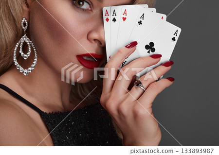 Blonde lady woman in black shiny dress and expensive diamond jewelry is winner money from Omaha Holdem. She is smiling, showing Aces cards to the camera. Ideal style for Poker, Casino, Gambling Blonde lady woman in black shiny dress and expensive diamond jewelry is winner money from Omaha Holdem. She is smiling, showing Aces cards to the camera. Ideal style for Poker, Casino, Gambling 133893987
