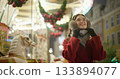 A young beautiful girl in a red coat walks in the evening at the European Christmas Market against the backdrop of a festive carousel with illuminations. 133894077