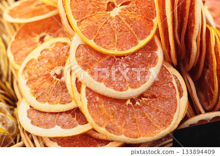 A basket full of dried citrus orange or grapefruit slices showcases their vibrant orange color and textured surface. These sweet-tart pieces are ideal for snacks or garnish. 133894409