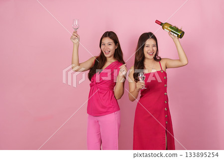 Party Vibes. Two women celebrating with drinks and a bottle in a playful atmosphere. Party Vibes. Two women celebrating with drinks and a bottle in a playful atmosphere. 133895254