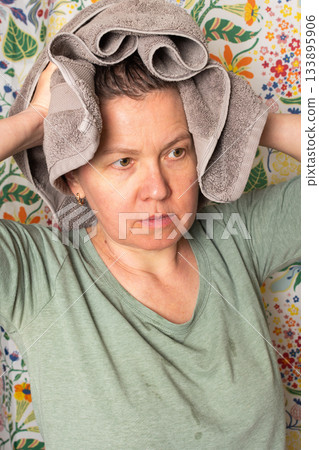 A 50-year-old woman stands in a vibrant bathroom, wrapping a towel around her head as she prepares for her morning routine. Flowers decorate the background, adding a lively touch 133895906