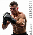 Intense Muscular Male Boxer in Fighting Stance Wearing Black Gloves Against Isolated White Background. 133895944