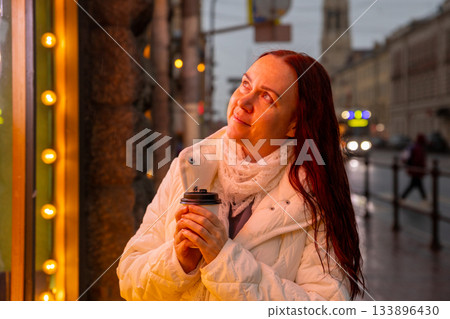 happy Caucasian woman drinks coffee in evening under neon lights. magical moment. happy Caucasian woman drinks coffee in evening under neon lights. magical moment. 133896430