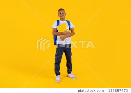 Preteen boy standing with notebook and backpack in bright yellow studio background Preteen boy standing with notebook and backpack in bright yellow studio background 133897473