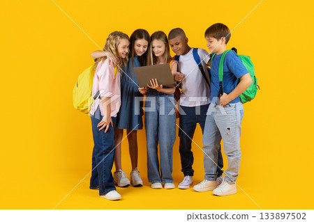 Preteen pupils standing close together with laptop, smiling and exploring digital learning 133897502