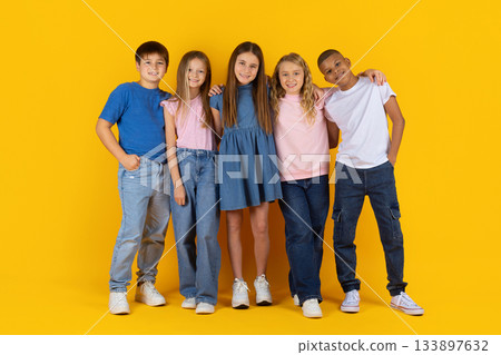 Preteen pupils standing close together and posing confidently in yellow studio background 133897632