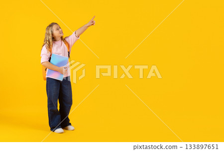 Preteen girl holding notebook and pointing upward on yellow studio background 133897651