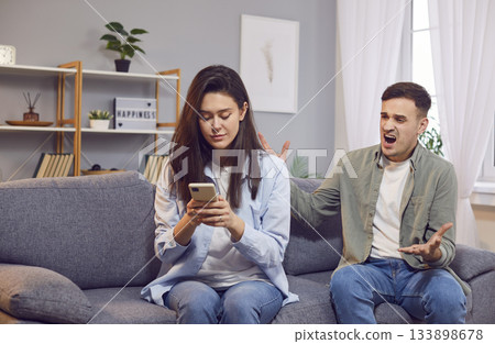 Quarreling young angry man shouting on his wife using mobile phone writing a message Quarreling young angry man shouting on his wife using mobile phone writing a message 133898678
