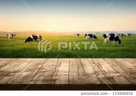 Empty wooden table top with cows in meadow and sunrise background. 133898858