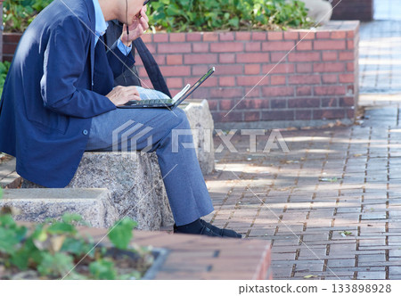 清晨,一位商人坐在公園長椅上看著他的筆記型電腦。 清晨,一位商人坐在公園長椅上看著他的筆記型電腦。 133898928