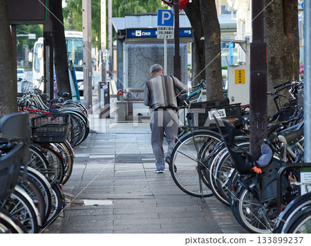 一位老人在名古屋市中心的自行車停車場推著自行車行走。 133899237