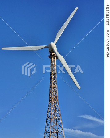 Vertical shot of a wind turbine. A tall, open lattice tower supports a three-bladed rotor 133899888