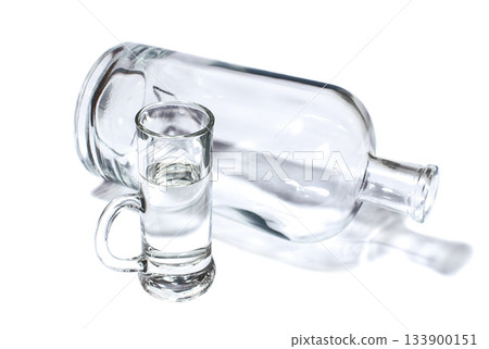 Bottle and small glass filled with transparent strong drink 133900151